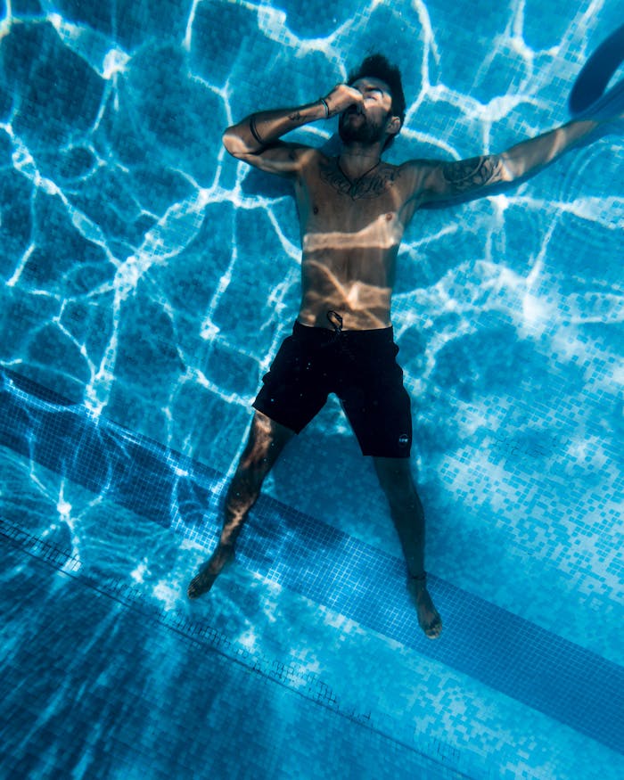 The Art of Drawing Readers In: Your attractive post title goes here Shirtless man with tattoos swimming underwater in a pool, enjoying leisure time.