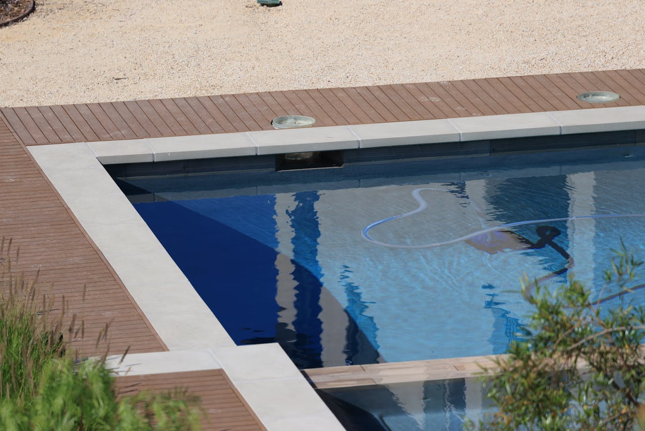 get-in-touch A serene swimming pool with wooden decking and clear blue water on a sunny day.