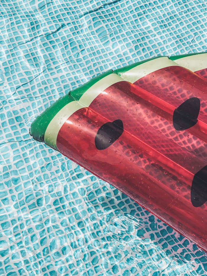 our-story A vibrant watermelon-shaped inflatable float on clear blue water in a swimming pool, perfect for summer leisure.