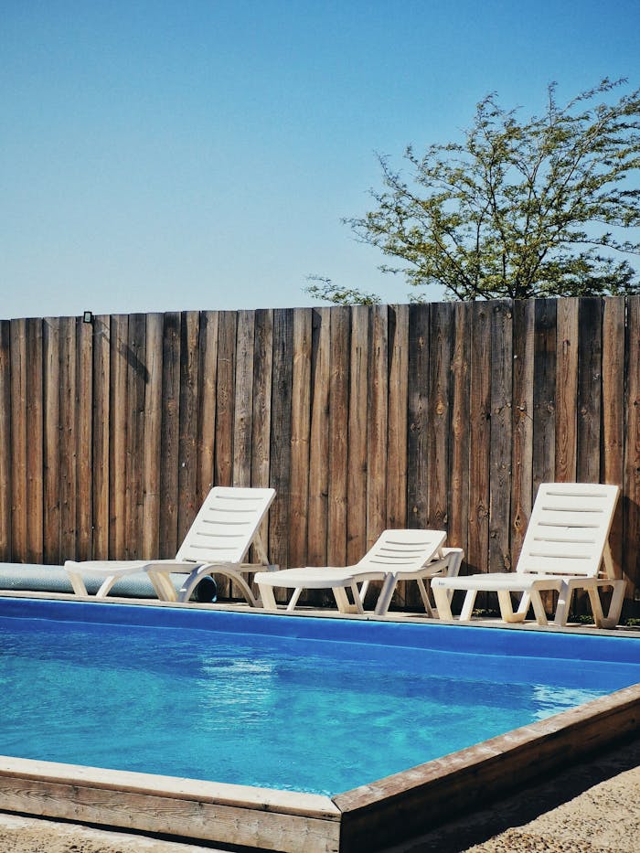 about-us Relax by the serene poolside with chairs and wooden fence on a sunny day.